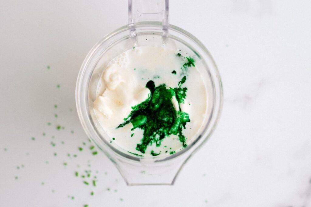 Green food coloring added to a blender filled with vanilla ice cream.