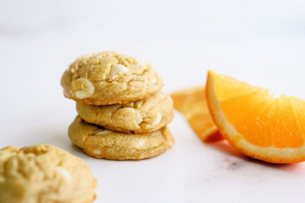 Orange Creamsicle Cookies stacked  with orange slices on the side.