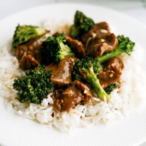 A white plate with slow cooker beef and broccoli served over white rice.