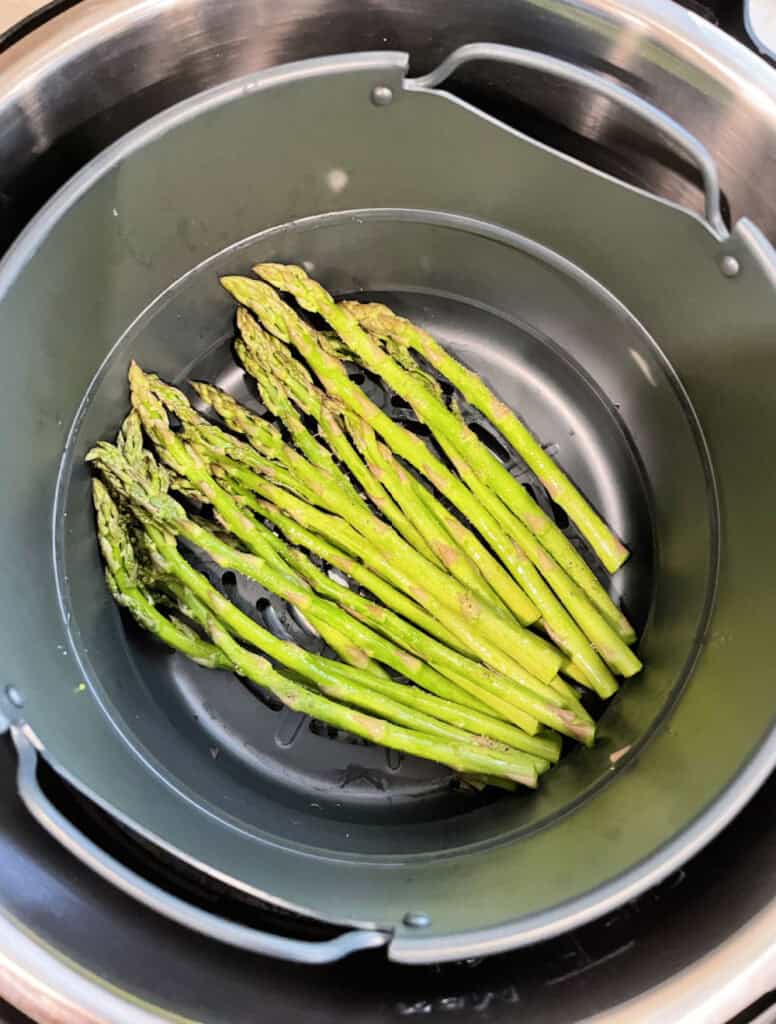 Seasoned and oiled asparagus in the bottom of an air fryer.