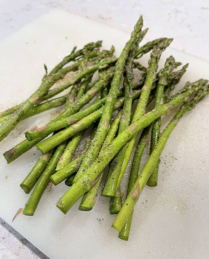 Fresh bunch of asparagus on a cutting board in a bunch seasoned and tossed with oil.