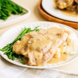 A white plate with Slow Cooker Pork Chops served over mashed potatoes with asparagus on the side.