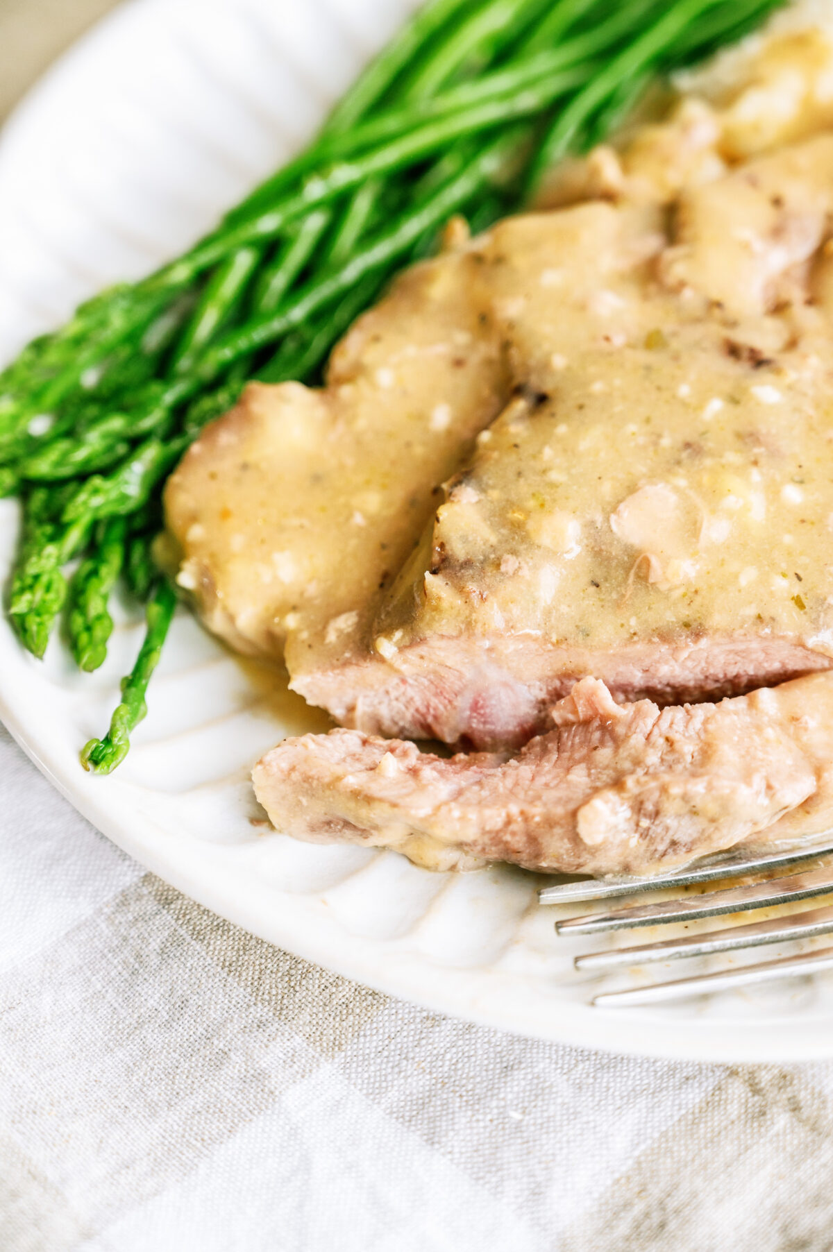 A Slow Cooker Pork Chop served over mashed potatoes on a plate with a slice of the pork chop next to a fork.