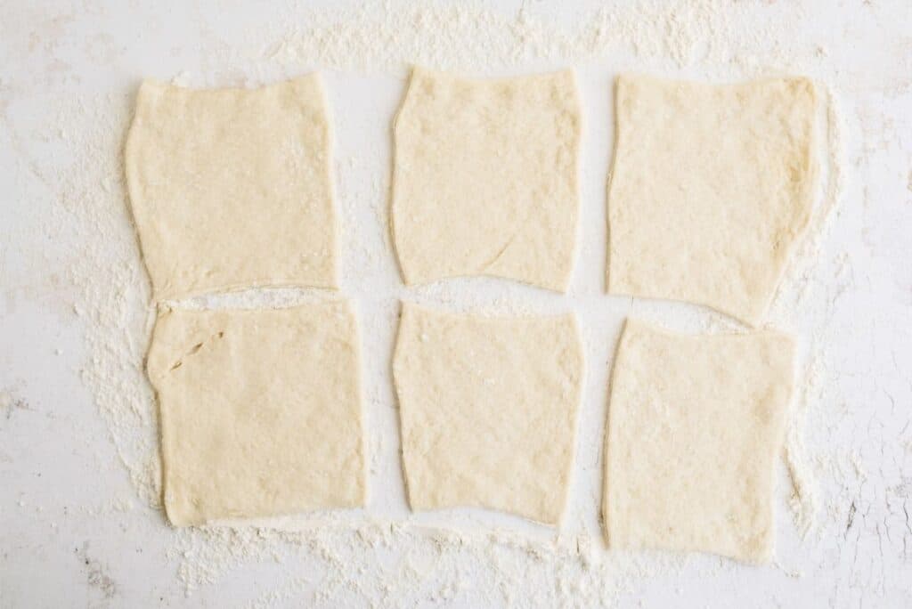 6 squares of pizza dough sitting on a counter top.