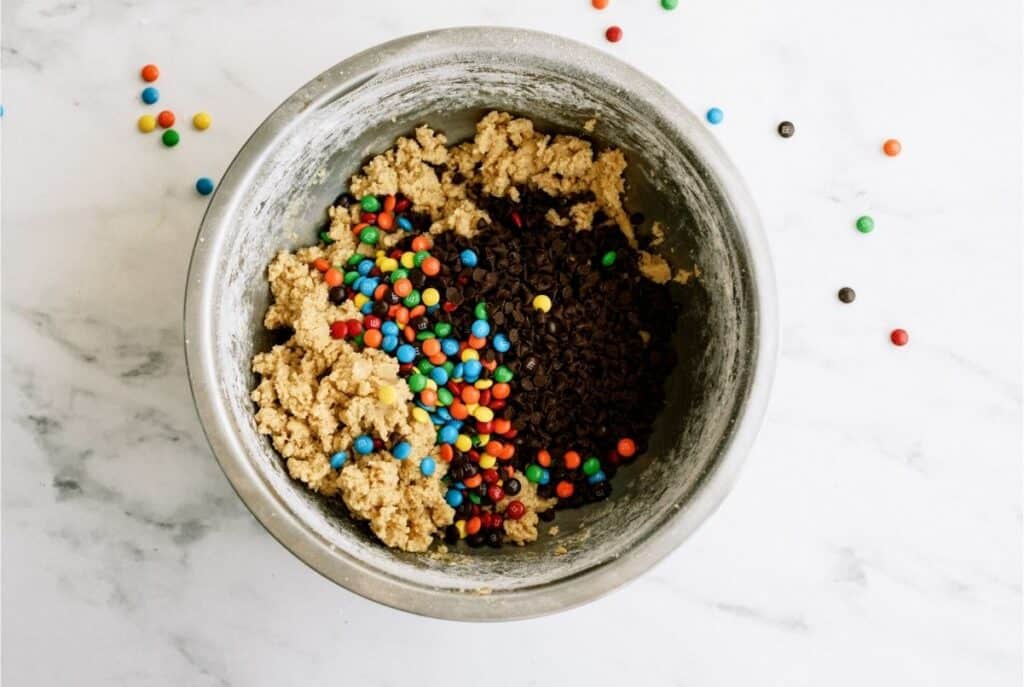 Adding M&M's to mixing bowl with cookie dough.