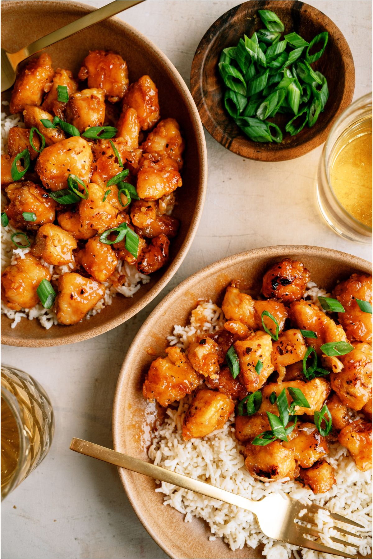 Close up of 2 plates of Baked Sweet and Sour Chicken served over white rice with a small bowl of garnish in the background.