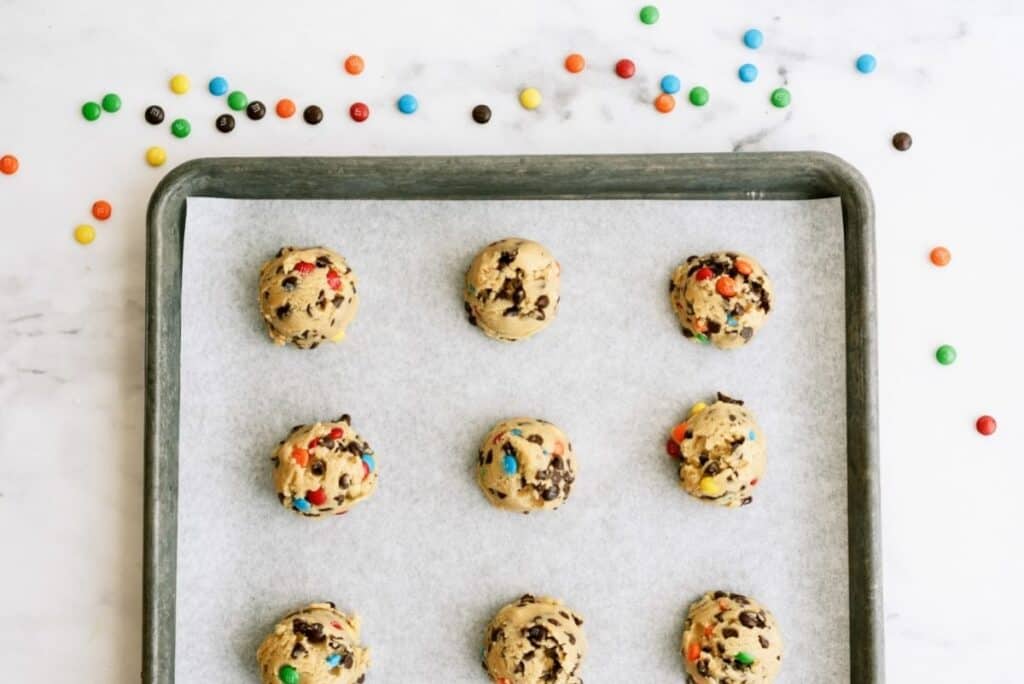 M&M Cookie dough balls on a lined baking sheet.