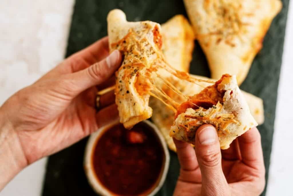 A hand breaking a Quick and Easy Calzones in half to show the inside.