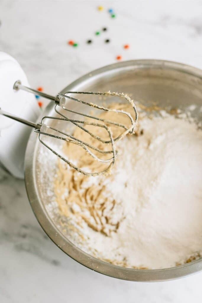 Ingredients for M&M Cookies in a mixing bowl with a hand mixer.