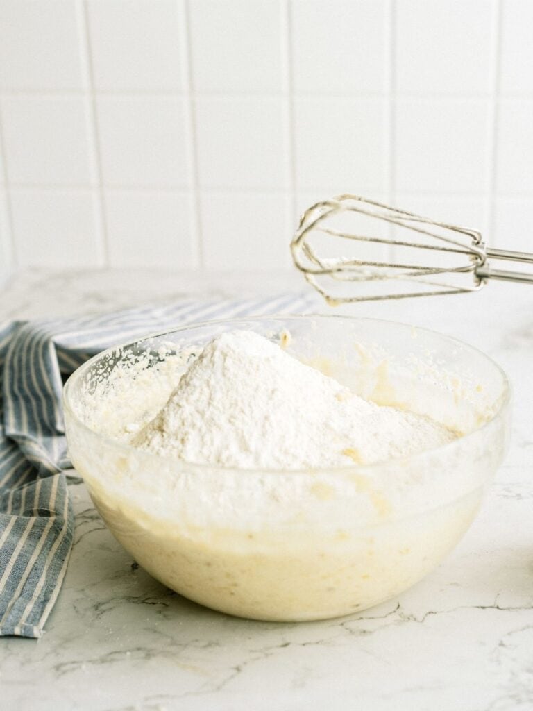 Adding dry ingredients to banana sugar mixture in mixing bowl.