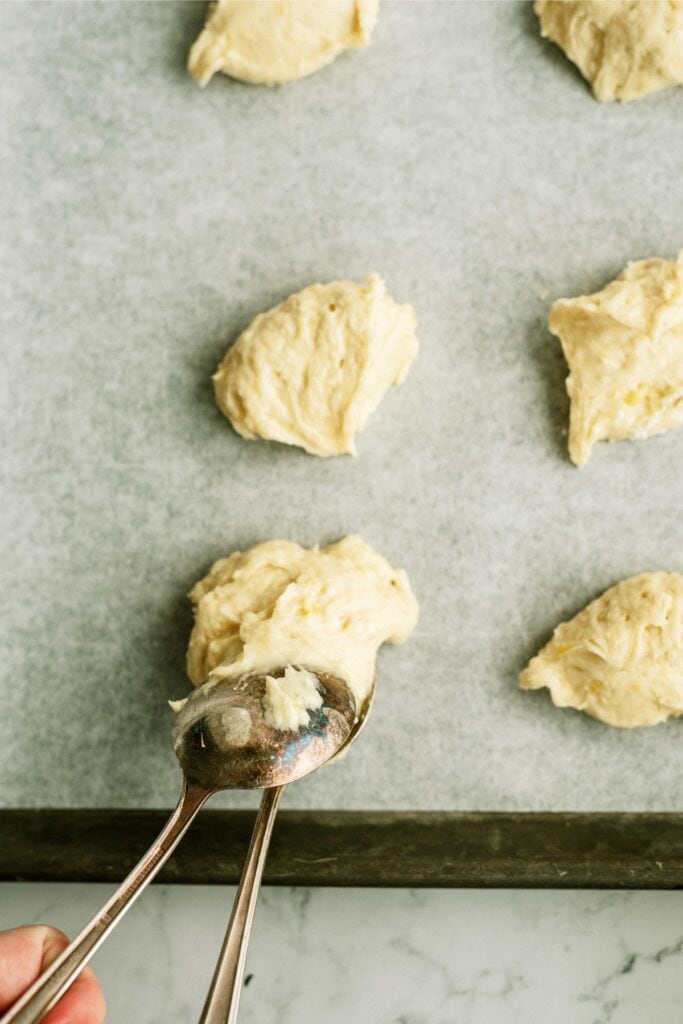 Spooning banana cookie dough onto a lined baking sheet.