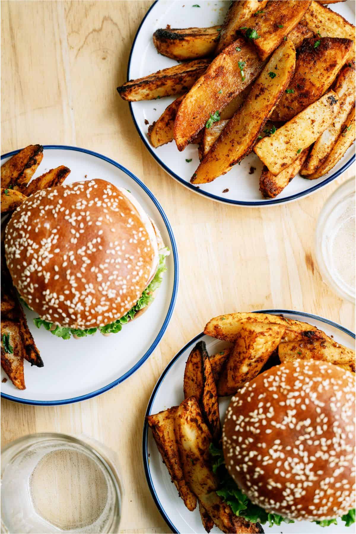 Top view of 2 plates with burgers and Oven Baked Seasoned Steak Fries and one plate of just Oven Baked Seasoned Steak Fries