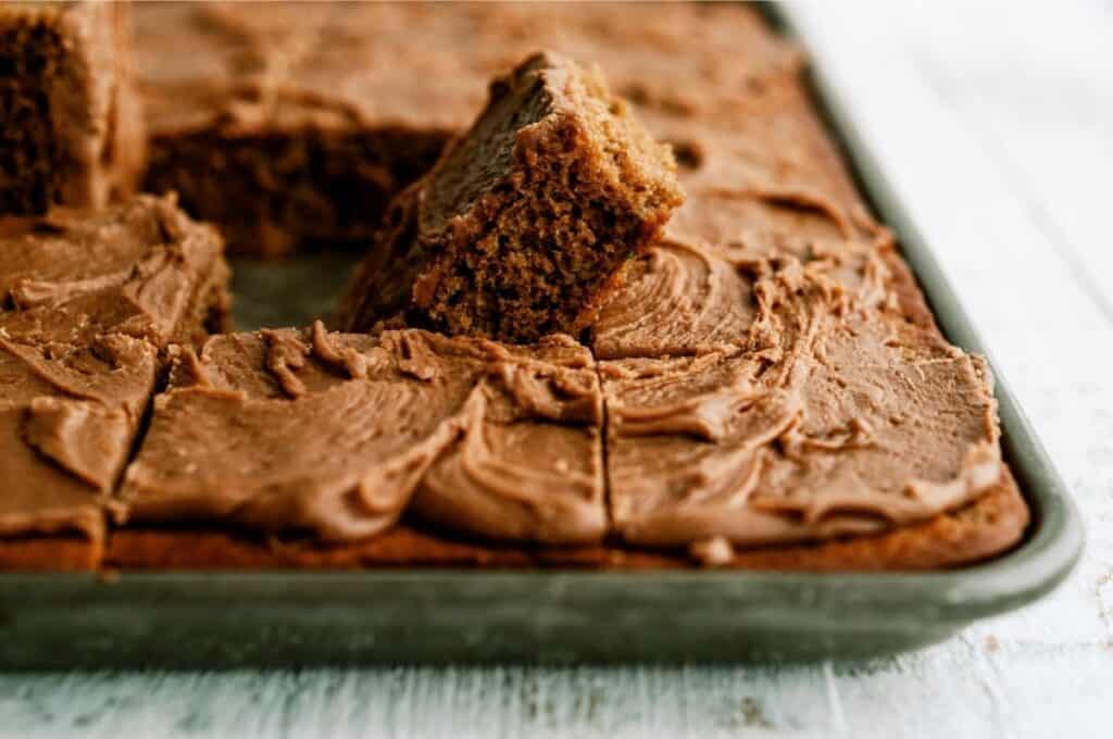 Frosted Chocolate Zucchini Sheet Cake cut into squares with one square being lifted up.