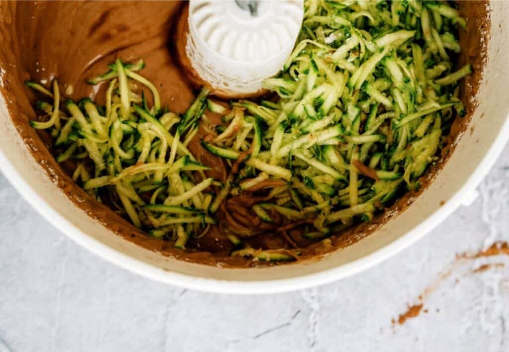 Shredded zucchini added to chocolate cake batter in a mixing bowl.