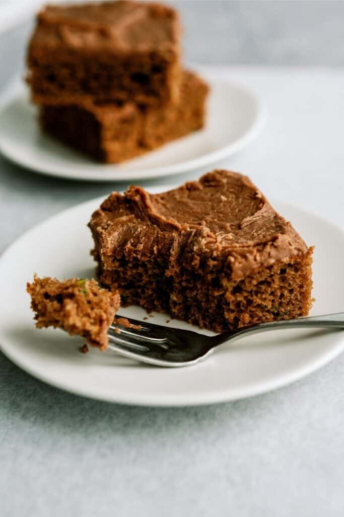 A slice of Chocolate Zucchini Sheet Cake on a plate with a fork holding a small bite of it.