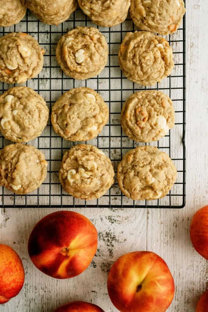 Peaches and Cream Oatmeal Cookies on a cooling rack surrounded by fresh peaches.