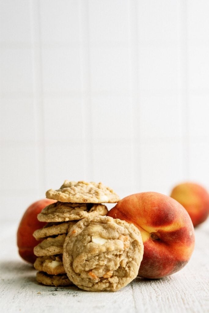 Stacked Peaches and Cream Oatmeal Cookies with fresh peaches in the background.