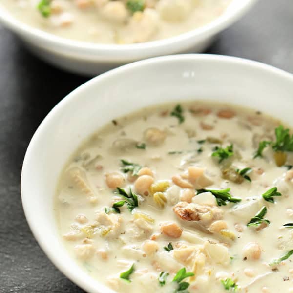Two white bowls filled with creamy chicken and rice soup, garnished with fresh herbs.
