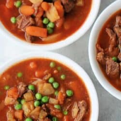 Three bowls of beef stew filled with chunks of meat, potatoes, carrots, and peas in a thick broth.