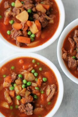 Three bowls of beef stew filled with chunks of meat, potatoes, carrots, and peas in a thick broth.