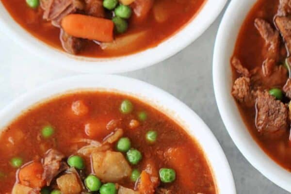 Three bowls of beef stew filled with chunks of meat, potatoes, carrots, and peas in a thick broth.