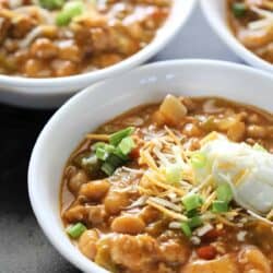 Three bowls of chicken chili topped with shredded cheese, sour cream, and chopped green onions.