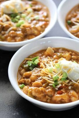 Three bowls of chicken chili topped with shredded cheese, sour cream, and chopped green onions.