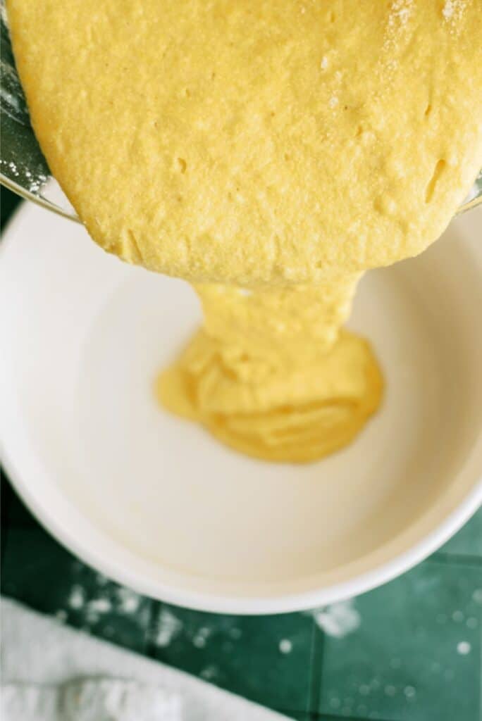 Pouring cornbread batter into a white baking dish.