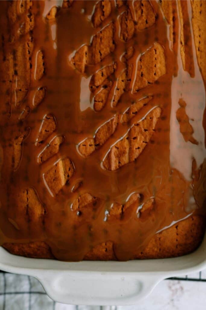 A close-up of a baked cake in a white dish, drizzled with caramel sauce.