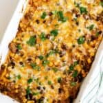 Baked casserole topped with melted cheese, black beans, corn, and fresh cilantro in a white dish.