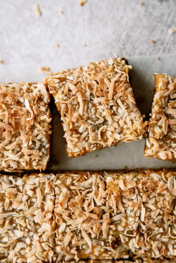 A rectangular white baking dish filled with a dessert topped with a layer of shredded coconut. The dish is lined with parchment paper.