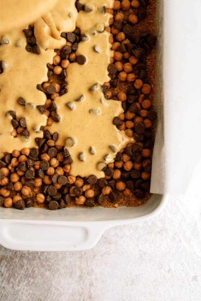 A baking dish filled with a mixture of chocolate chips, caramel chips, and a creamy batter being poured on top.