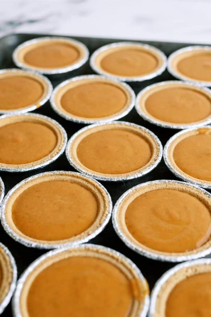 Several neatly arranged mini pumpkin pies in foil tins are displayed on a dark tray.