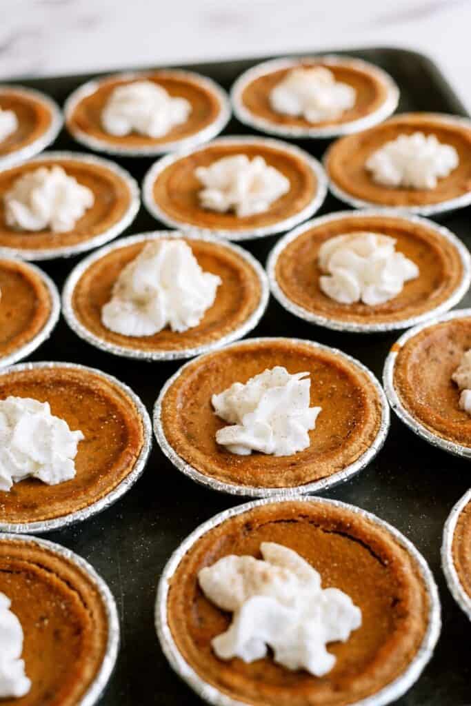 A tray of mini pumpkin pies topped with dollops of whipped cream arranged in rows.