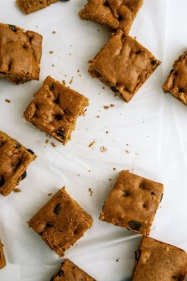 Several square-cut pieces of baked bar cookies lie on a white surface, with a few crumbs scattered around.