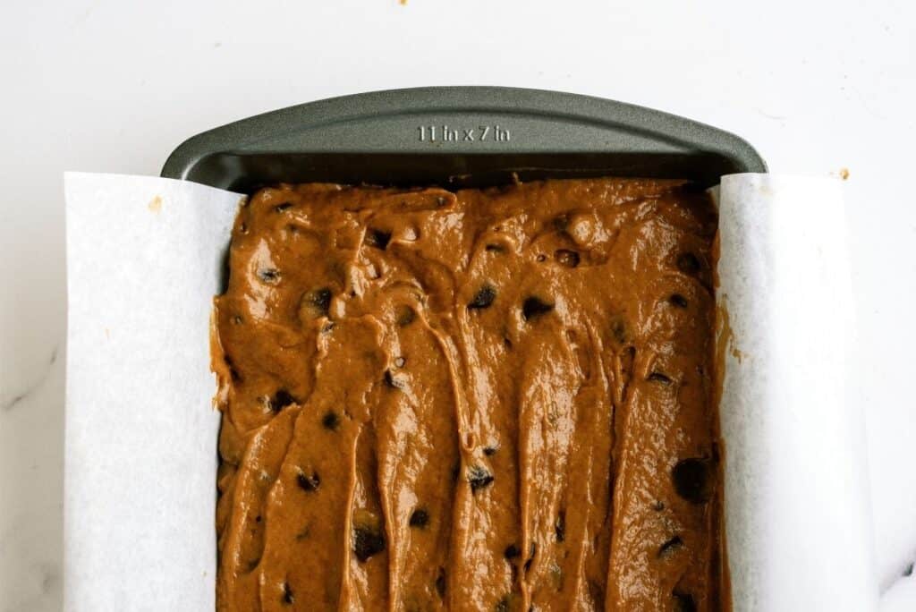 Loaf pan filled with unbaked chocolate chip batter on a white countertop.