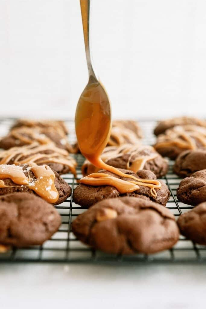 A spoon drizzling melted caramel on top of baked cookies.