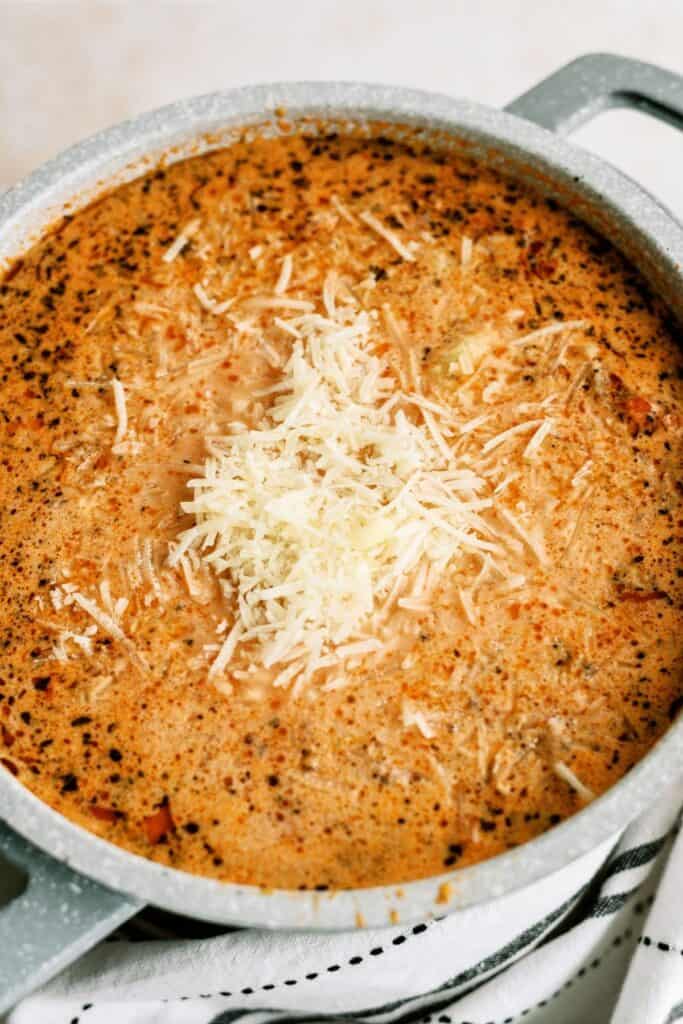 A pot filled with creamy tomato basil soup, topped with grated cheese.