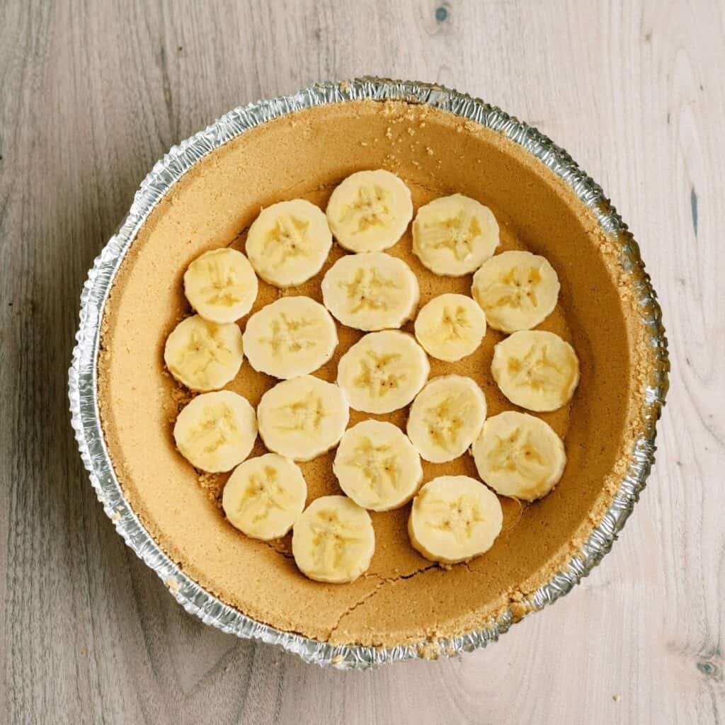 A layer of sliced bananas on the bottom of a graham cracker pie crust.