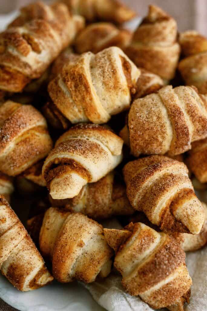 A close-up image shows a pile of golden-brown, sugar-dusted croissants stacked together.