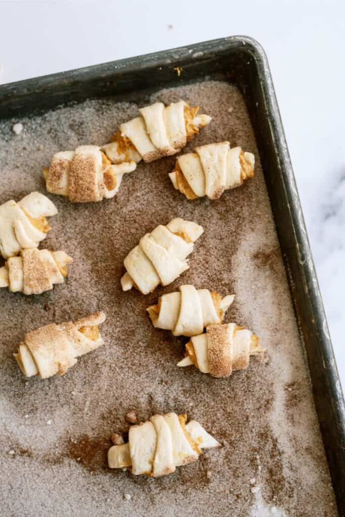 Unbaked crescent rolls filled with apple slices and sprinkled with cinnamon sugar are arranged on a baking sheet.