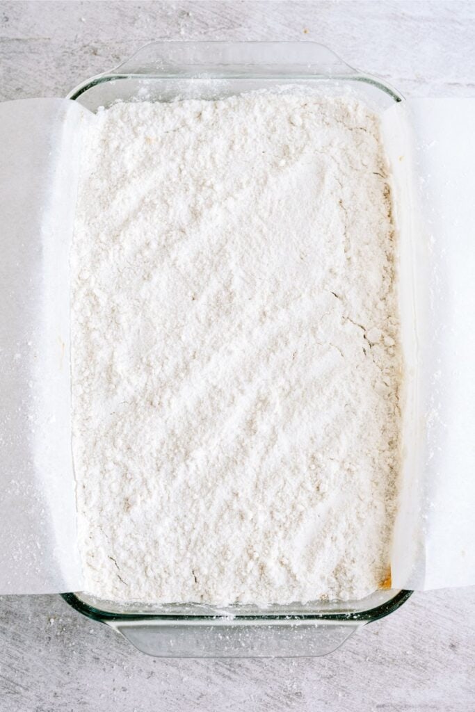 A glass baking dish filled with a layer of white powdery flour, lined with parchment paper, placed on a light gray surface.