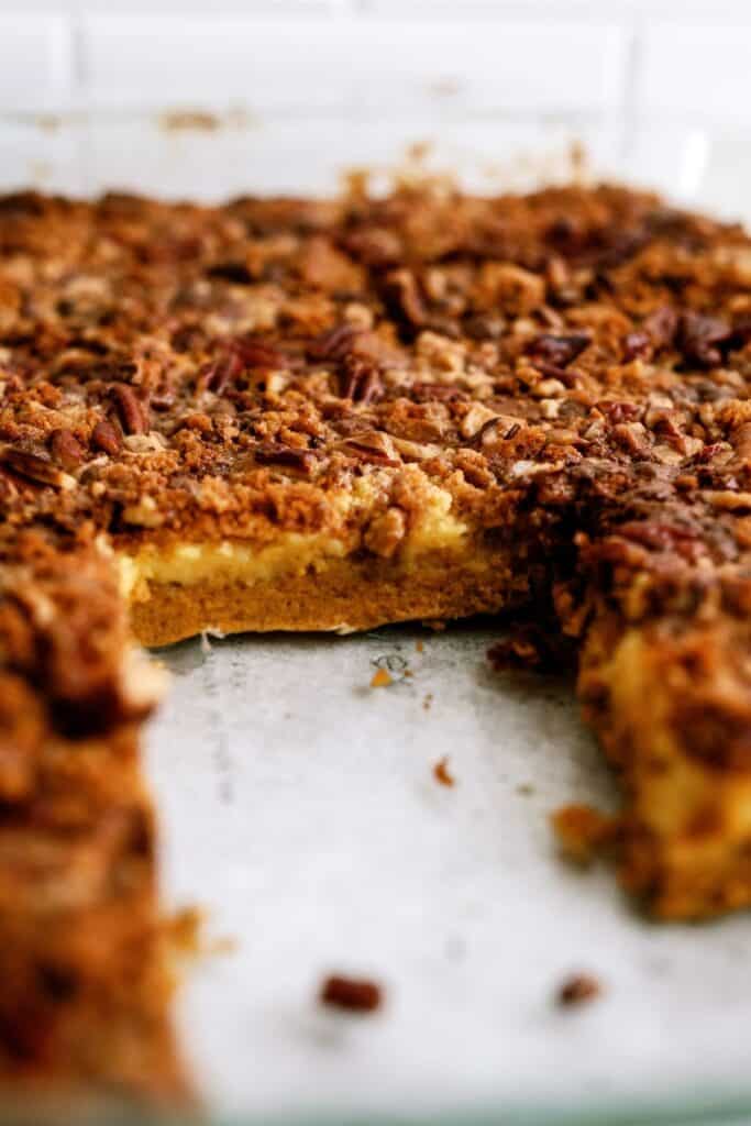 A baked dessert with a crumbly topping, featuring a missing piece that reveals a layered, creamy interior.