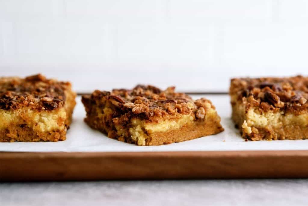 Close-up view of three pieces of crumb-topped baked bars on a parchment-lined baking sheet.