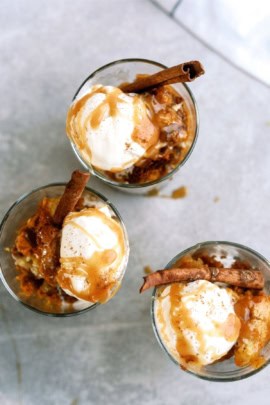 Three glass cups filled with a dessert, each topped with a scoop of vanilla ice cream, caramel sauce, and a cinnamon stick.