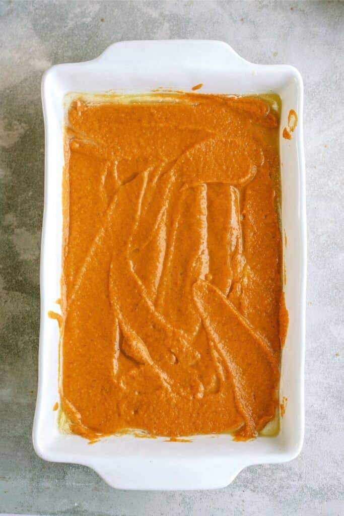 A white rectangular baking dish filled with a smooth, orange batter placed on a grey surface.