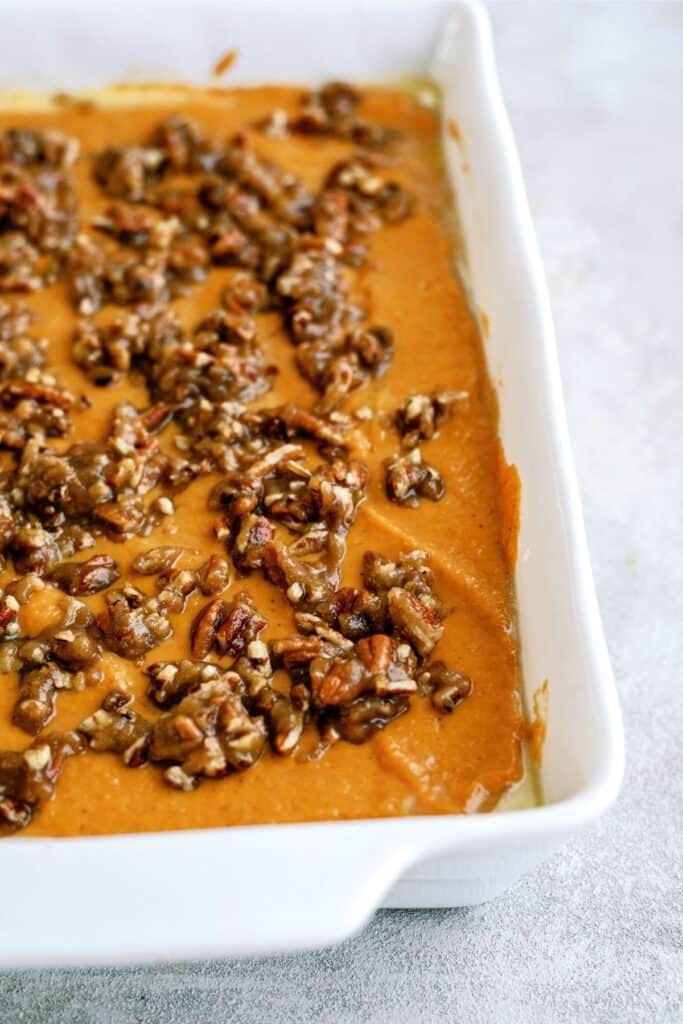 A white rectangular dish filled with a baked sweet potato casserole topped with pecans.