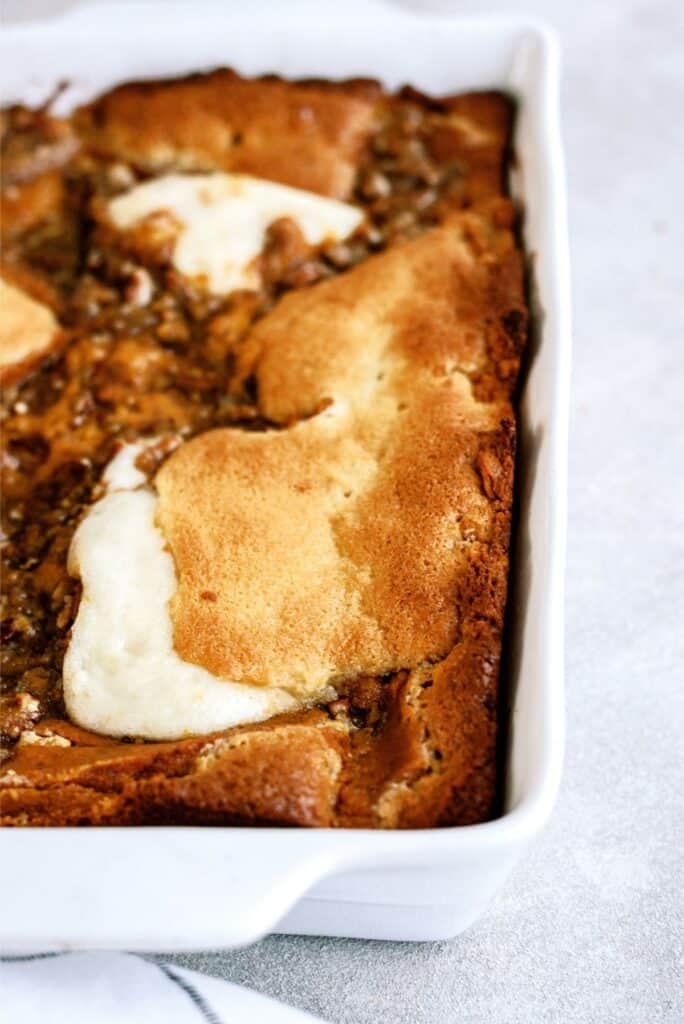 A close-up of a rectangular baked dessert with a golden-brown crust and white cream cheese patches in a white baking dish.