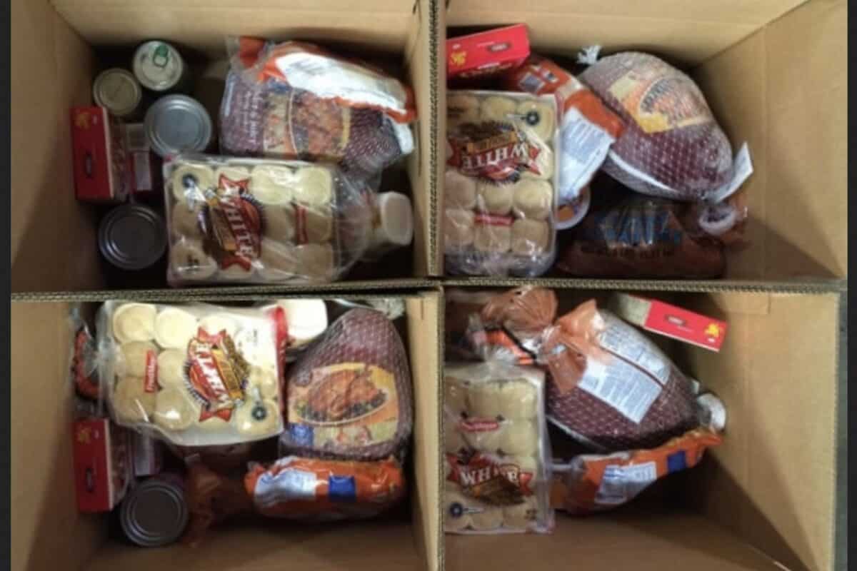 Four cardboard boxes filled with various food items including canned goods, bread, packaged meat, and other groceries.