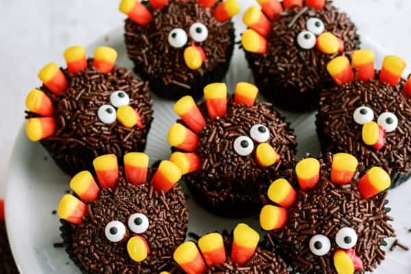 Chocolate cupcakes decorated to resemble turkeys, with candy corn feathers and candy eyes, arranged on a white plate.